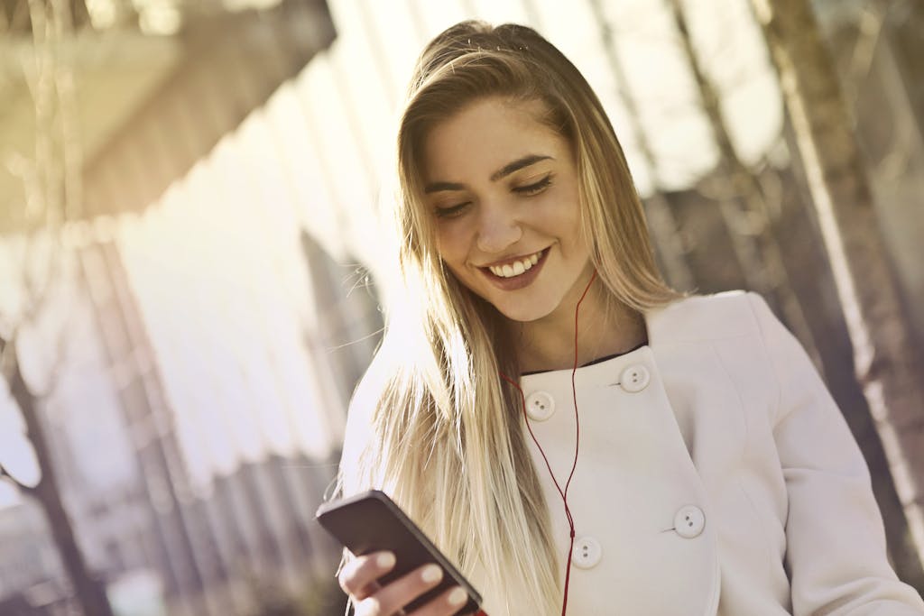 Happy woman listening to music on her smartphone with earphones while walking outdoors.